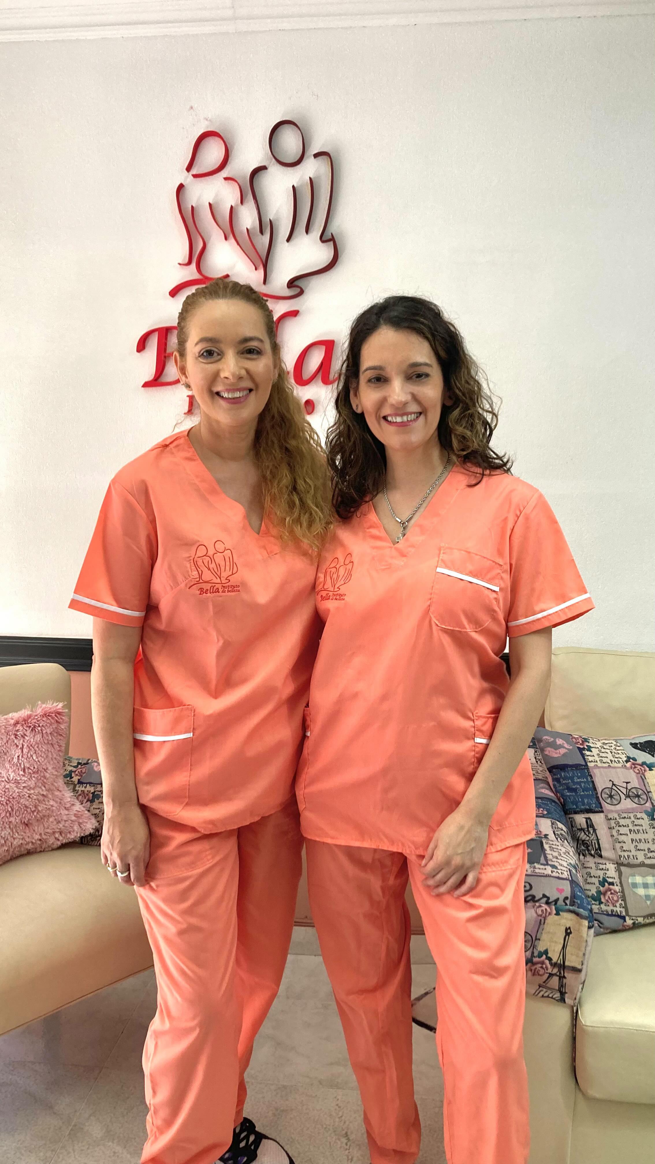 Dos integrantes del equipo de Bella con uniforme coral, sonriendo frente al logo rojo de la recepción